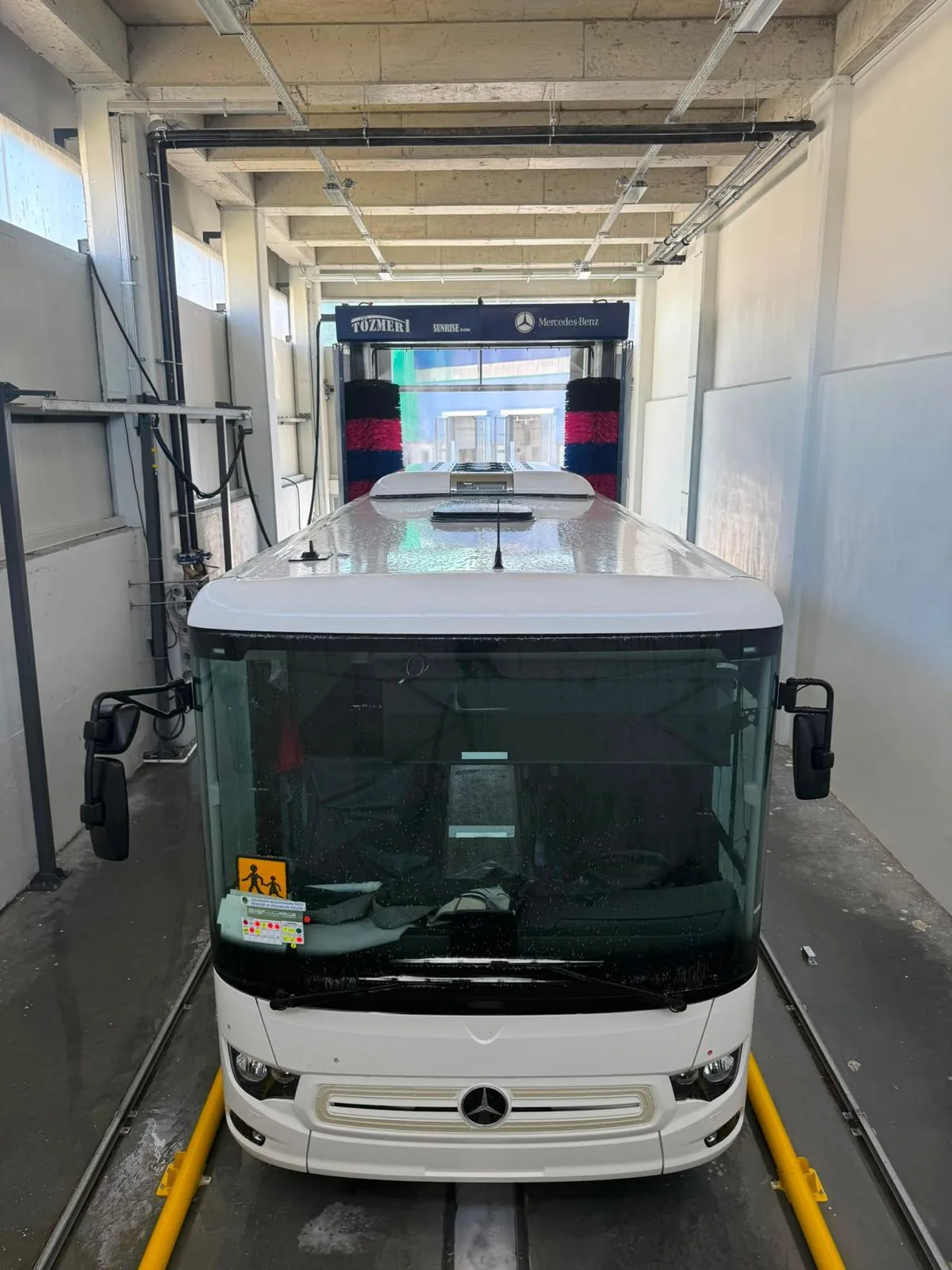 White coach driving into a wash gantry inside an enclosed wash hall, with floor guides on each side